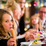 Ein Mädchen sitzt mit seiner Familie an Weihnachten am Esstisch und ist ein Wiener Würstchen. Auf ihrem Teller liegt Kartoffelsalat. Leckeres Weihnachtsessen.