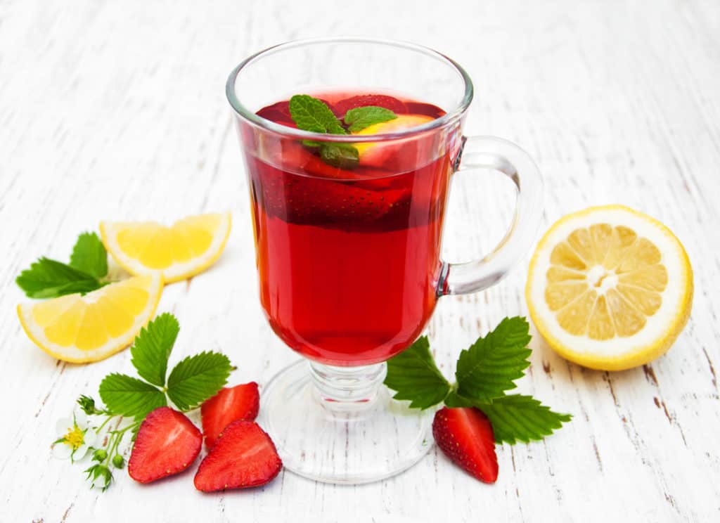 Erbeerbowle im Glas mit daneben liegenden Erdbereeren, Zitronen und Zirtonenmelisse dekoriert.