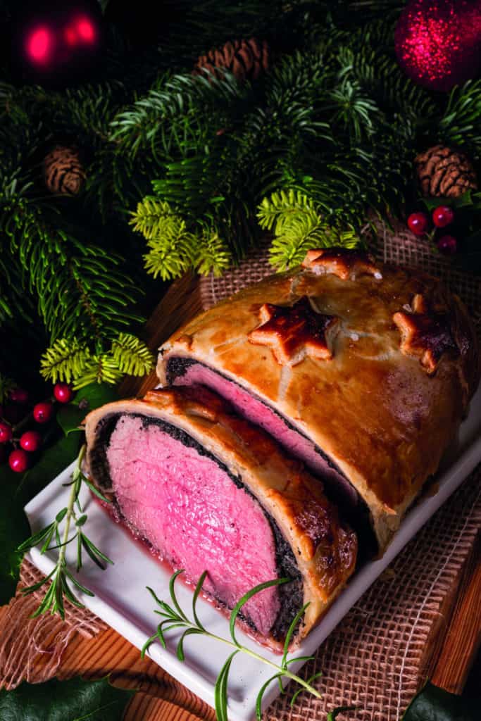 Beef Wellington zu Weihnachten, ein ganzes Rinderfiflet im Blätterteigmantel, aufgeschnitten auf dem weihnachtlich dekorierten Esstisch.