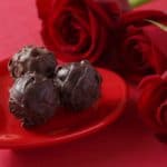 Eine kleine rote Herzschale mit Schokoladenkugeln und einem Strauß roter Rosen
