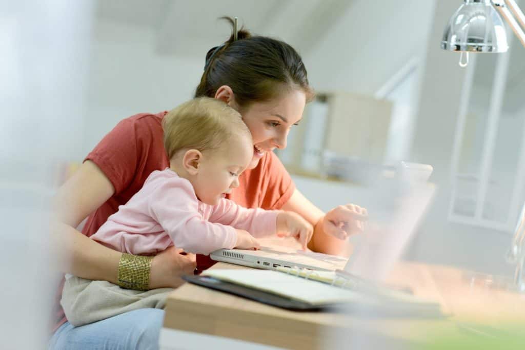 Homeoffice: Frau arbeitet mit Baby auf dem Schoss am Laptop.