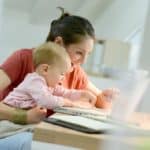 Homeoffice: Frau arbeitet mit Baby auf dem Schoss am Laptop.