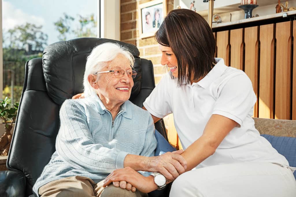 Pfegefachkräfte: Seniorin sitzt im Sessel nehmen einer sympatischen jungen Pflegerin.