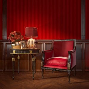 Rot bezogener Ledersessel und Tisch mit Goldverzierungen passen perfekt zu einer Wandgestaltung aus naturbelassenem und rot gestrichenem Holz.