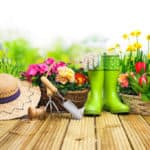 Sommerhut, grüne Gummistiefel, Gartenwerkzeug und bunte Blumen in Körben: Alles für ein neues Bluemenbeet