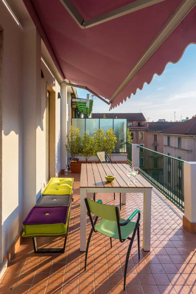 Halbausgefahrene rote Markise über einem Balkon, auf dem ein Tisch und mehrere Sitzgelegenheiten stehen.