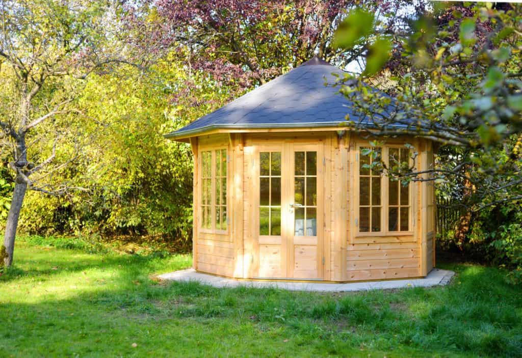 Ein hölzernes secheckiges Gartenhaus mit großen Fenstern steht im Garten.