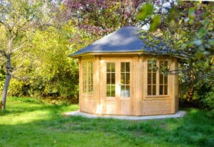 Ein hölzernes secheckiges Gartenhaus mit großen Fenstern steht im Garten.