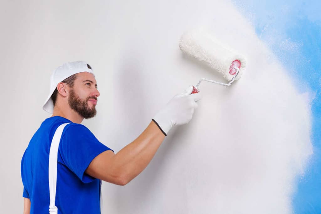 Handwerker mit blauem T-Shirt streicht eine Wand weiß.