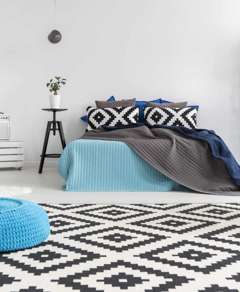 Schlafzimmer, in dem die Muster der Kissen auf den Teppich und die Farbe des Poufs auf die Tagesdecke abgestimmt sind.