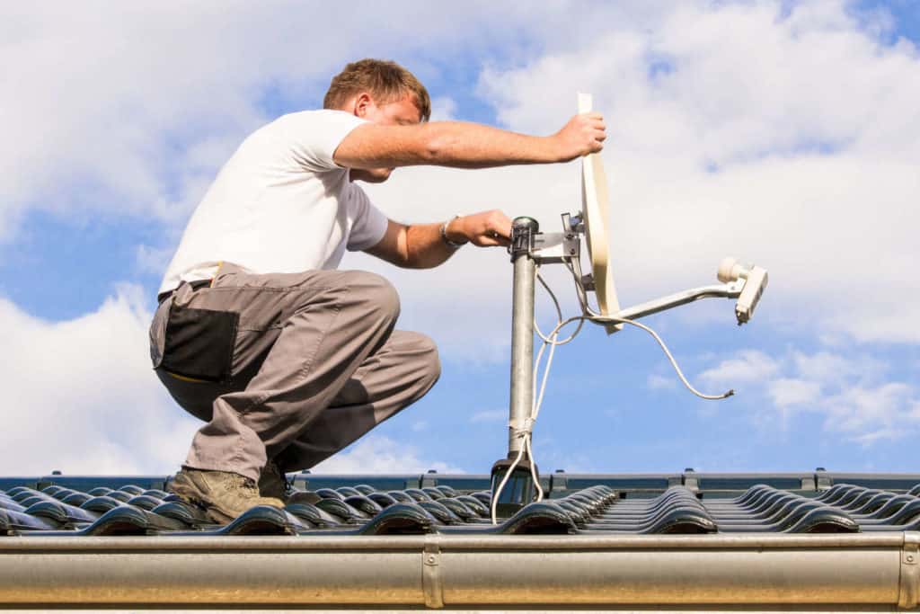 Handwerker überprüft auf dem Dach die Satellitenschüssel. Winterchek für das Haus