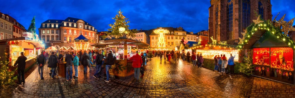 Adventsbräuche: Der Heidelberger Weihnachtsmarkt mit seinen Ständen und Besuchern als Panoramaaufnahme.