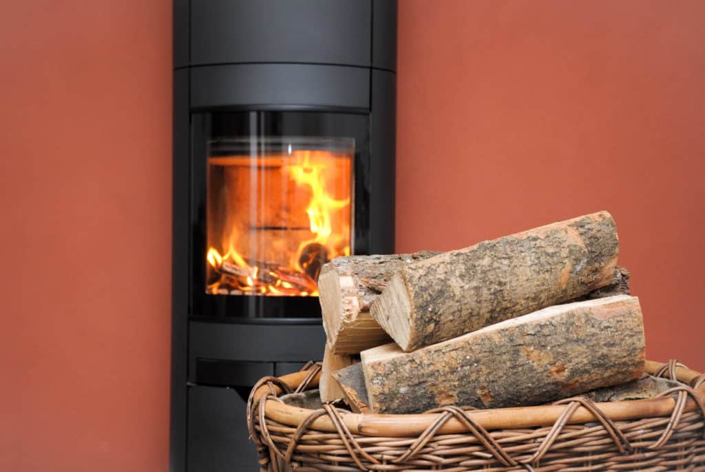 Feuer in schwarzem Kaminofen. Davor ein Korb mit Brennholz für den Kamin.