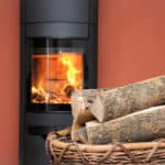 Feuer in schwarzem Kaminofen. Davor ein Korb mit Brennholz für den Kamin.