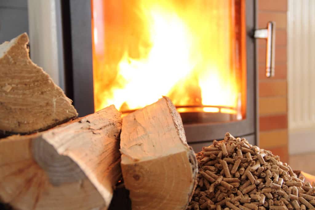 Pelletofen mit lodernden Flammen. Davor Holzscheite und Pellets. Brennholz für den Kamin.
