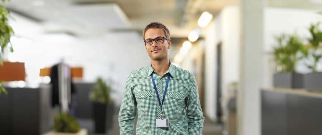 Junger Mann mit Hemd und Brille vor hellen Büroräumen.