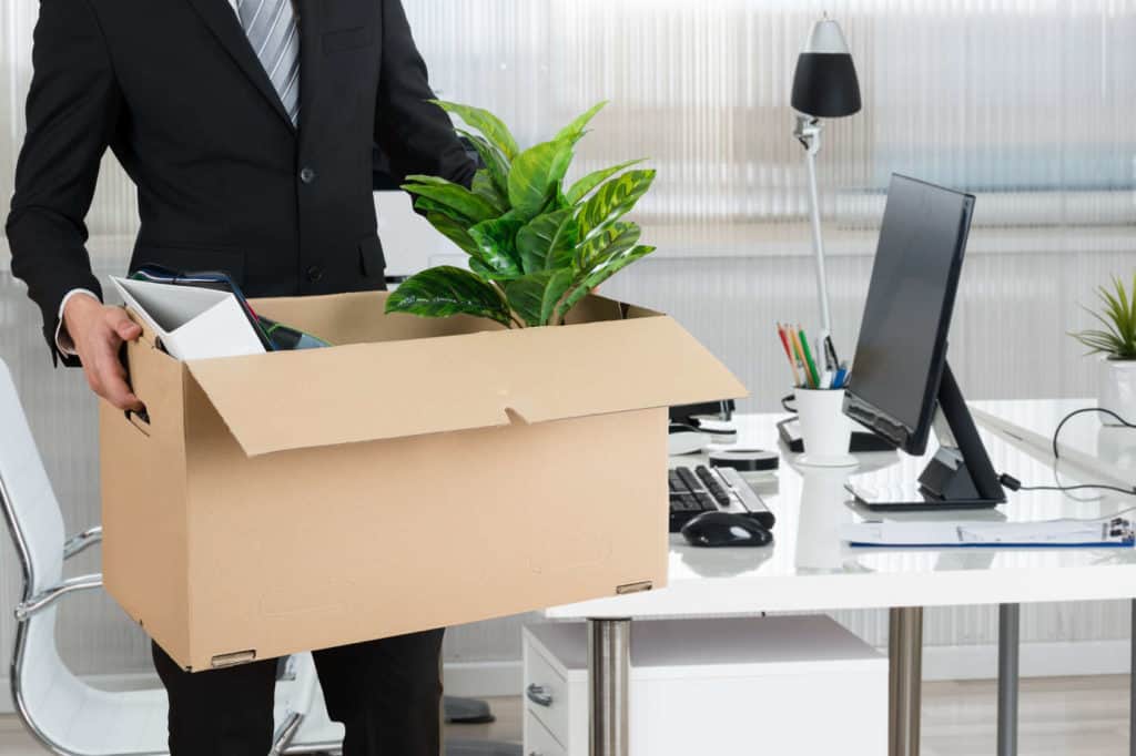 Job-Bewertungen: Ein Angestellter trägt einen Karton mit seinen Büroutensilien.