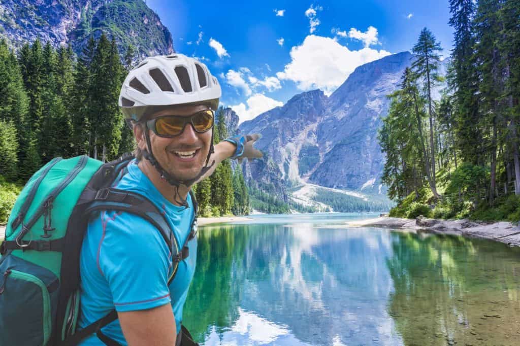 Radreise: Radler in sportlicher Radlerkleidung mit Helm vor einem See und Gebirge.
