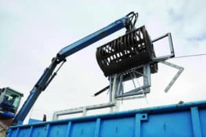 Nach dem Fensteraustausch: Ein Bagger hebt mehrere alte Fensterprofile in einen blauen Container.