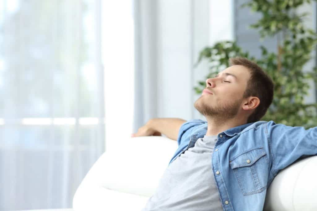 Junger Mann lehnt sich entspannt auf einem Sofa zurück – Allein reisen