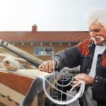 Ein Klempner mit Schnurbart montiert auf einem Dach eine Regenrinne