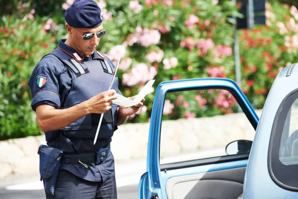 Urlaub mit dem eigenen auto: Italienischer Polizist prüft die Papiere am Auto.