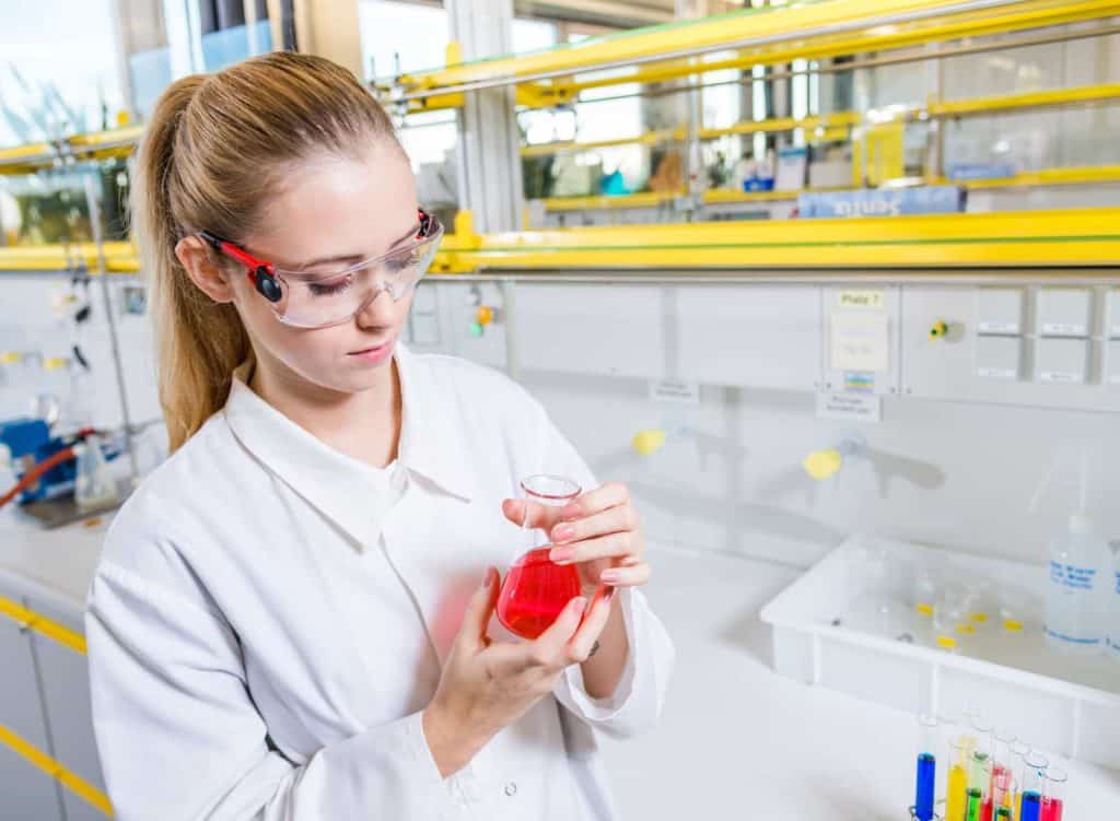 Junge Frau in einem Labor in weißem Kittel mit Schutzbrille - Mädchen im Männerberuf