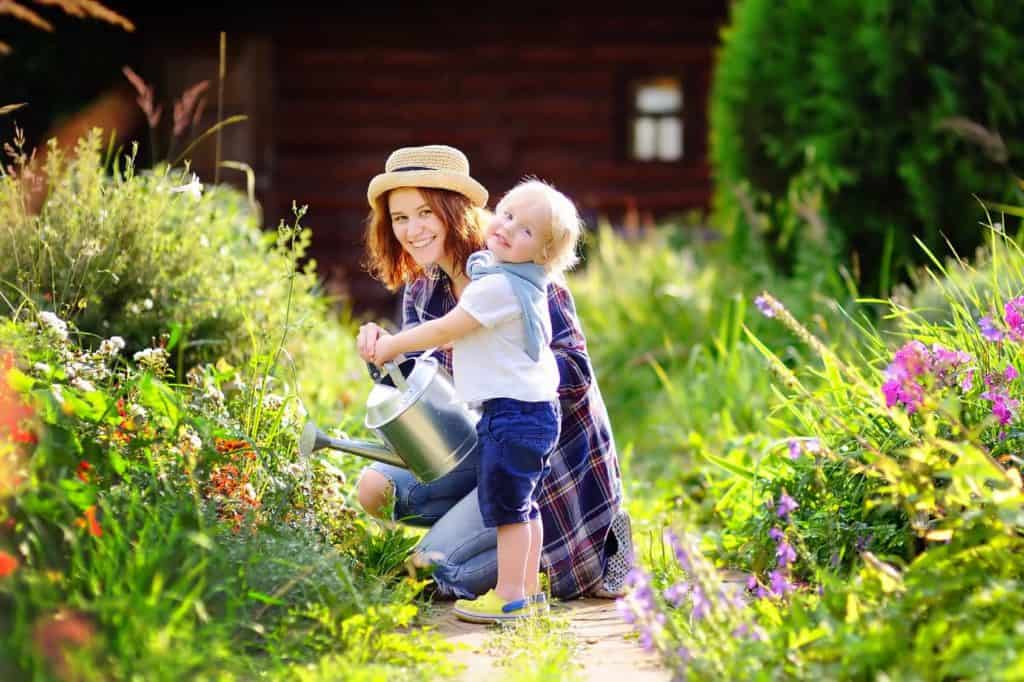 Cottage Gärten - kleines Kind gießt mit seiner Mutter Blumenstauden.