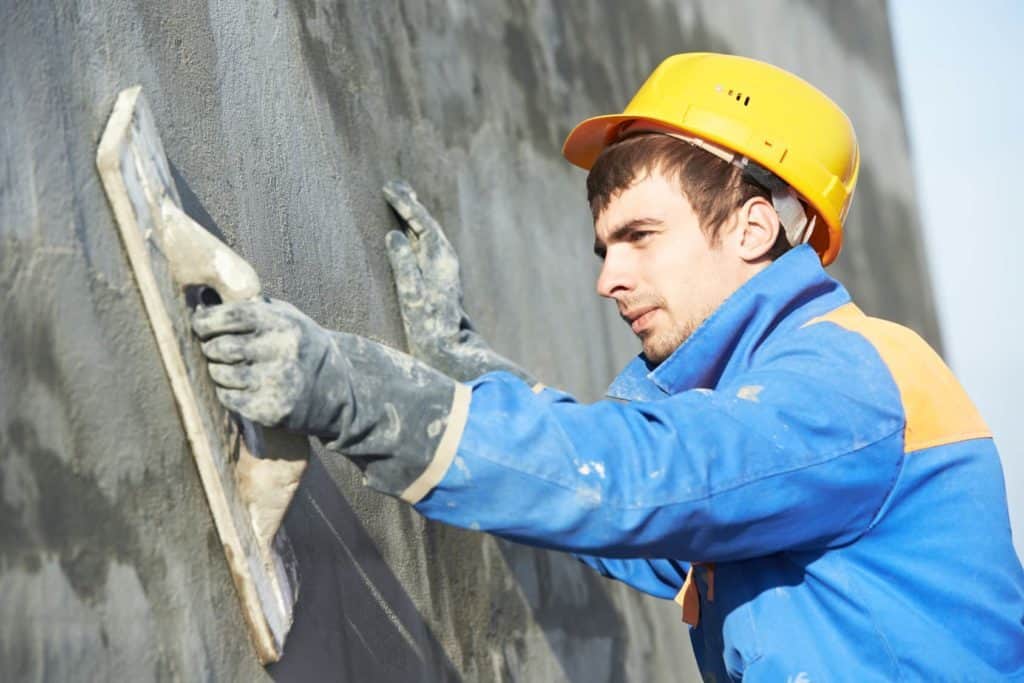 Ein junger Mann trägt Putz auf eine Hauswand auf.