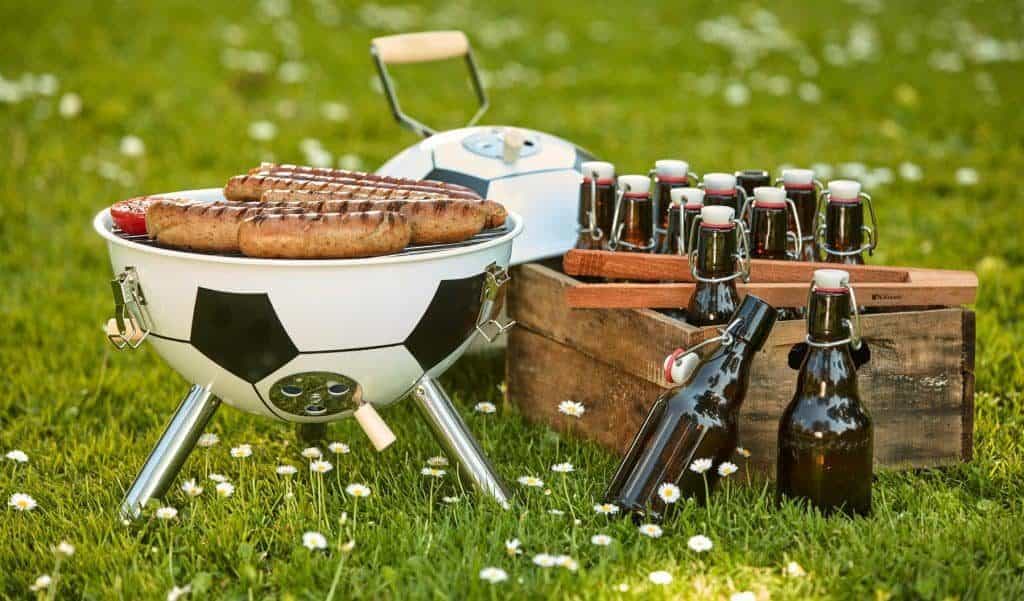 Kleiner Fußballgrill mit Würstchen und Bier auf dem Rasen (So gelingt die WM-Party im Garten)