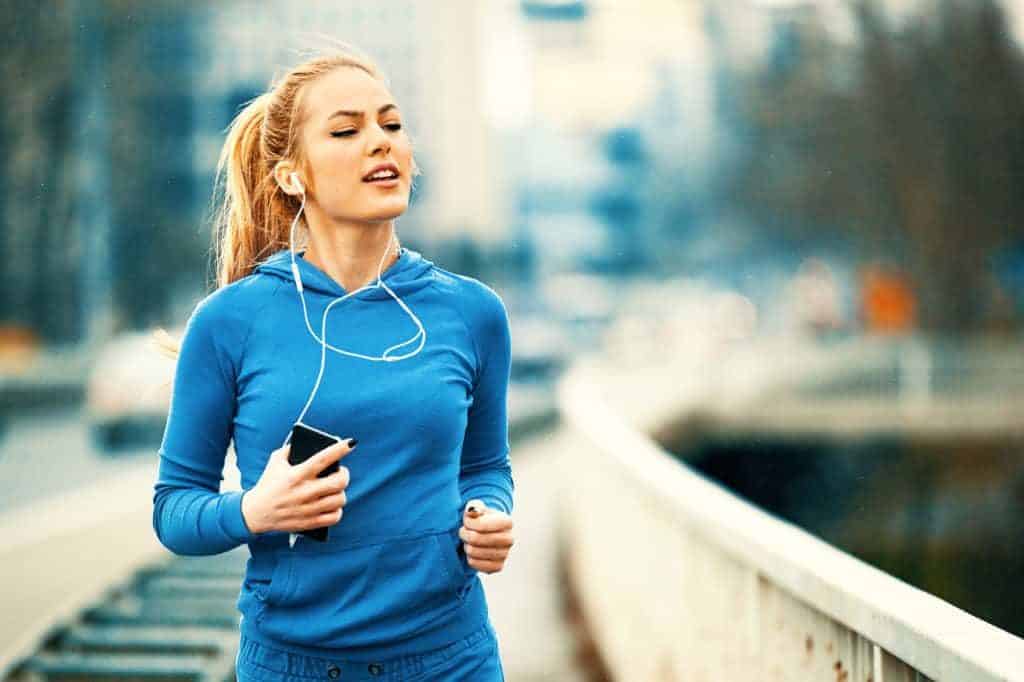 Joggen für Anfänger: Junge Frau im Blauen Trainingsanzug mit Smartphnone und Kopfhörern beim Joggen.