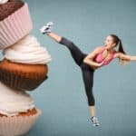 Eine Frau tritt gegen einen überdimmensionalen Turm aus Cupcakes.(Fitness-Mythen)