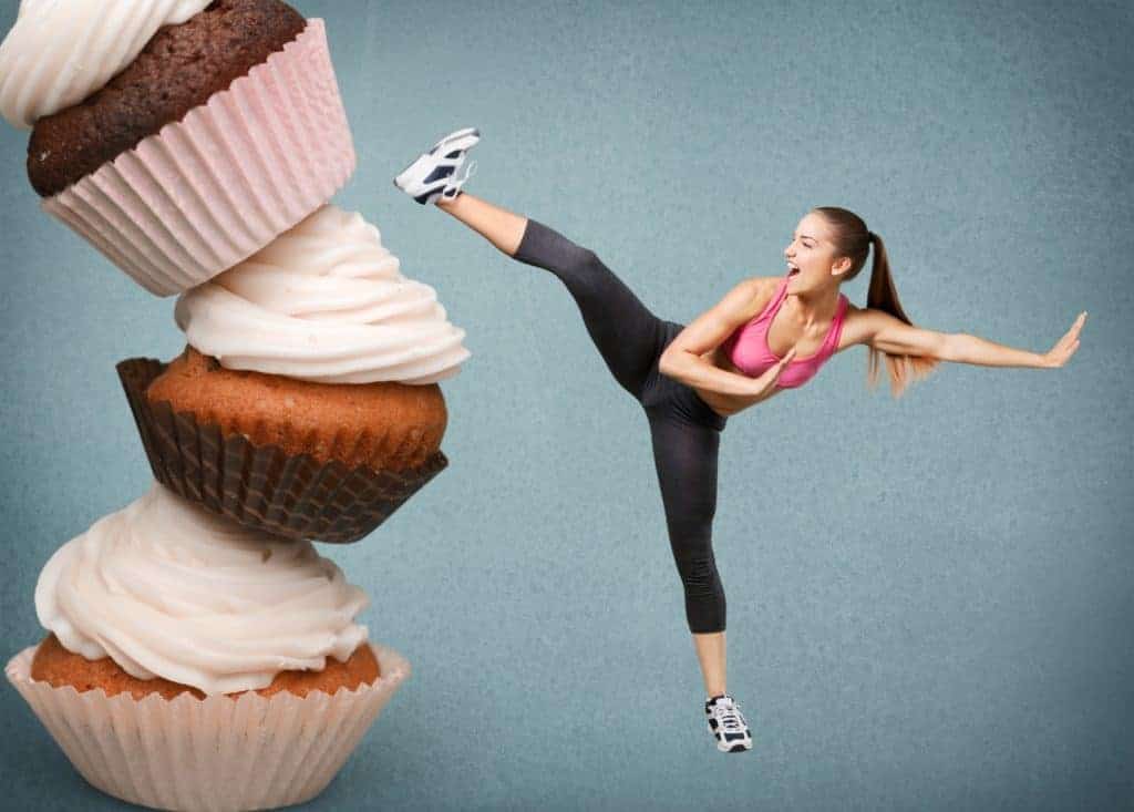 Eine Frau tritt gegen einen überdimmensionalen Turm aus Cupcakes.(Fitness-Mythen)