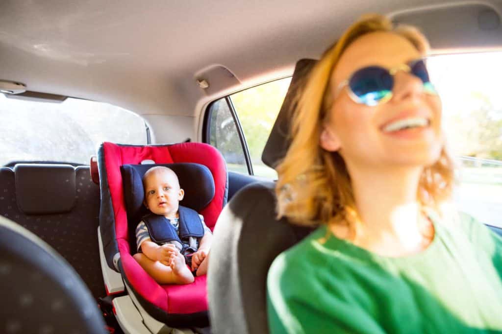 Eine junge Mutter betrachtet während der Fahrt ihr Kind auf der Rückbank durch den Rückspiegel.