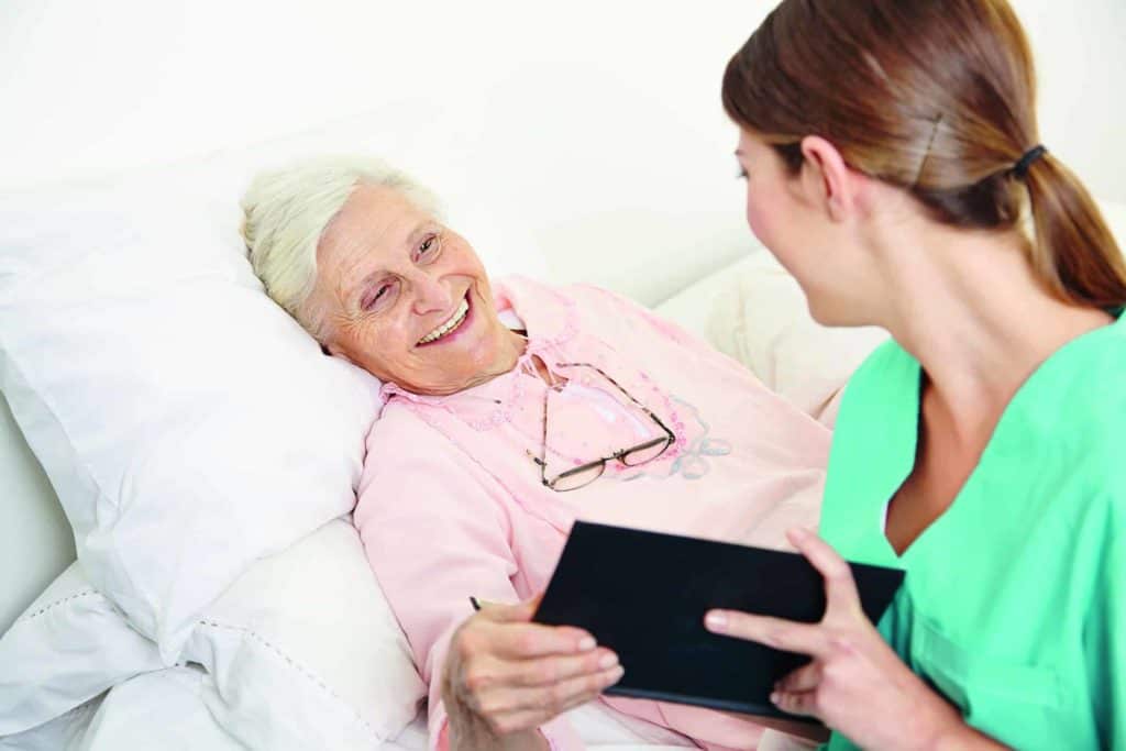 Pflegerin am Bett einer älteren Patientin (Pflegekräfte in der Zeitarbeit)