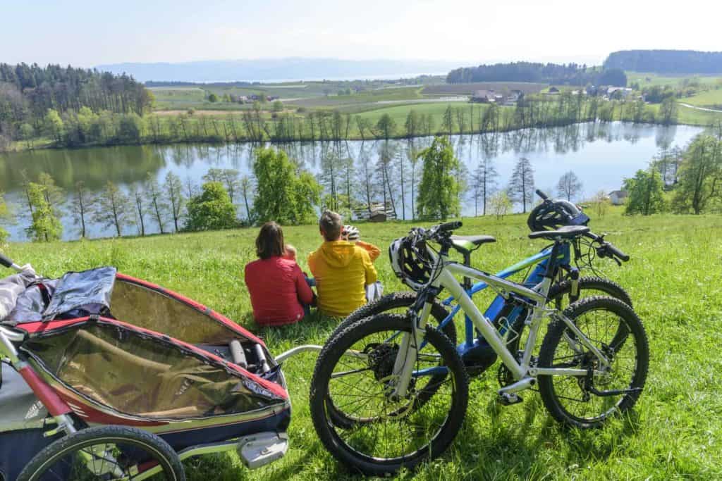 Eine Familie sitzt mit ihren Fahrrädern an einem See. (Urlaub zuhause genießen)