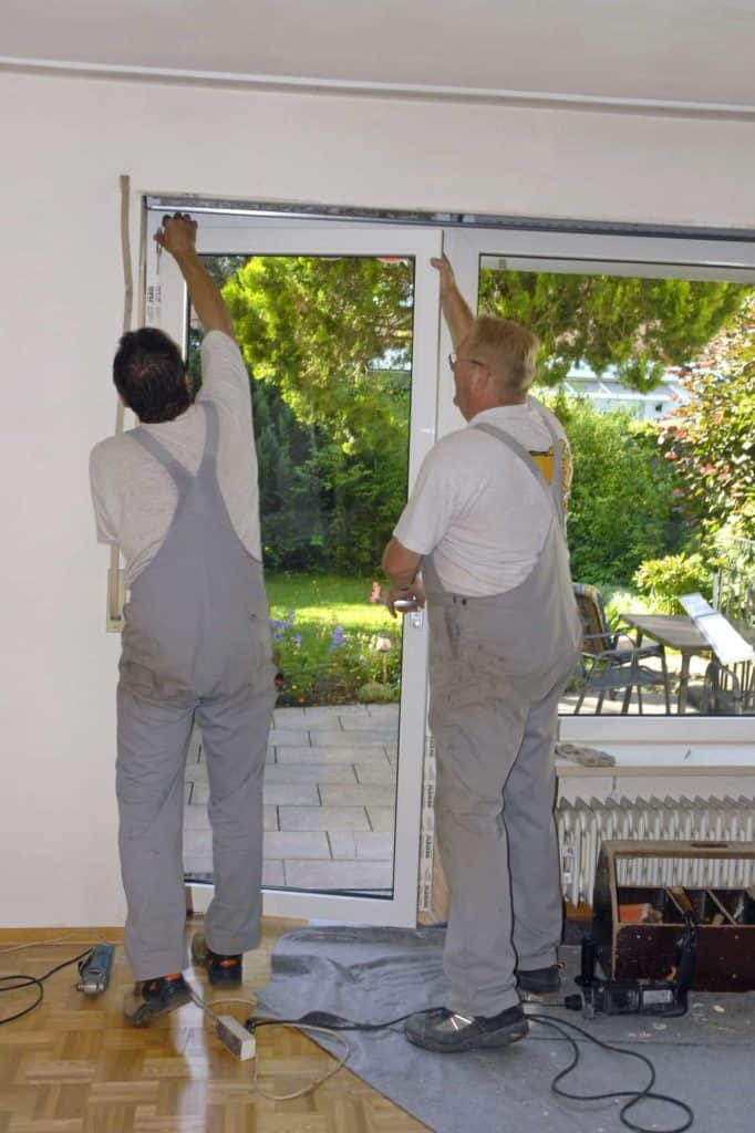 Fenstertausch: Einhängen der neuen Terrassentür durch zwei Handwerker.