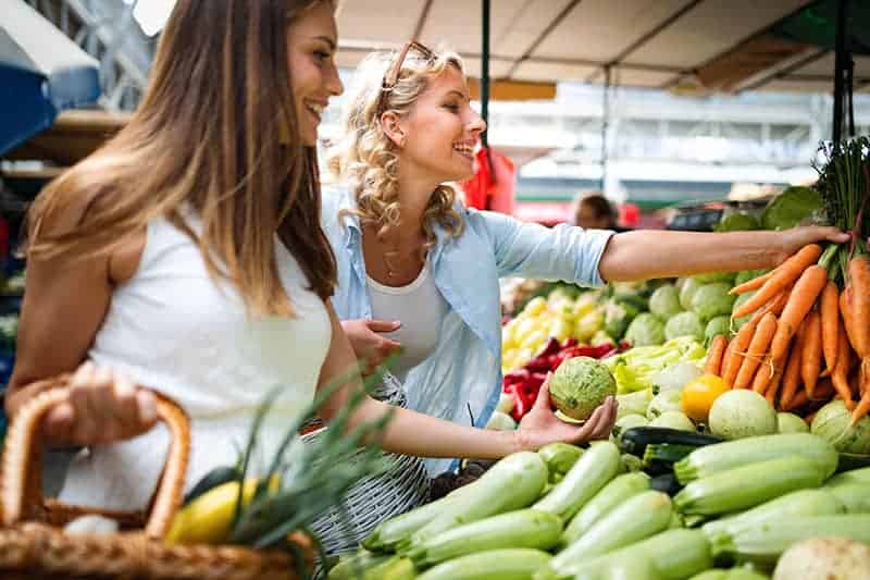 Nachhaltig einkaufen: zwei junge Frauen kaufen frisches Obst und Gemüse.
