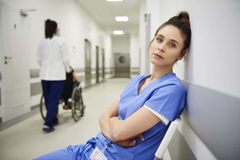 Midlife Crisis Frauen: Krankenschwester sitzt auf einer bank und denkt nach.