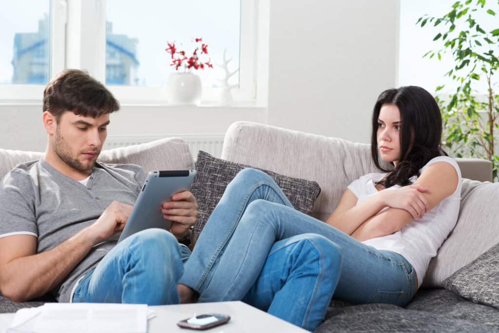 Workaholic: ein Paar sitzt gemeinsam auf einem Sofa, doch der Mann schaut auf sein Tablet.