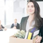 Lächelnde Arbeitnehmerin hält eine Kiste mit persönlichen Sachen, nachdem sie ihren Job gekündigt hat.