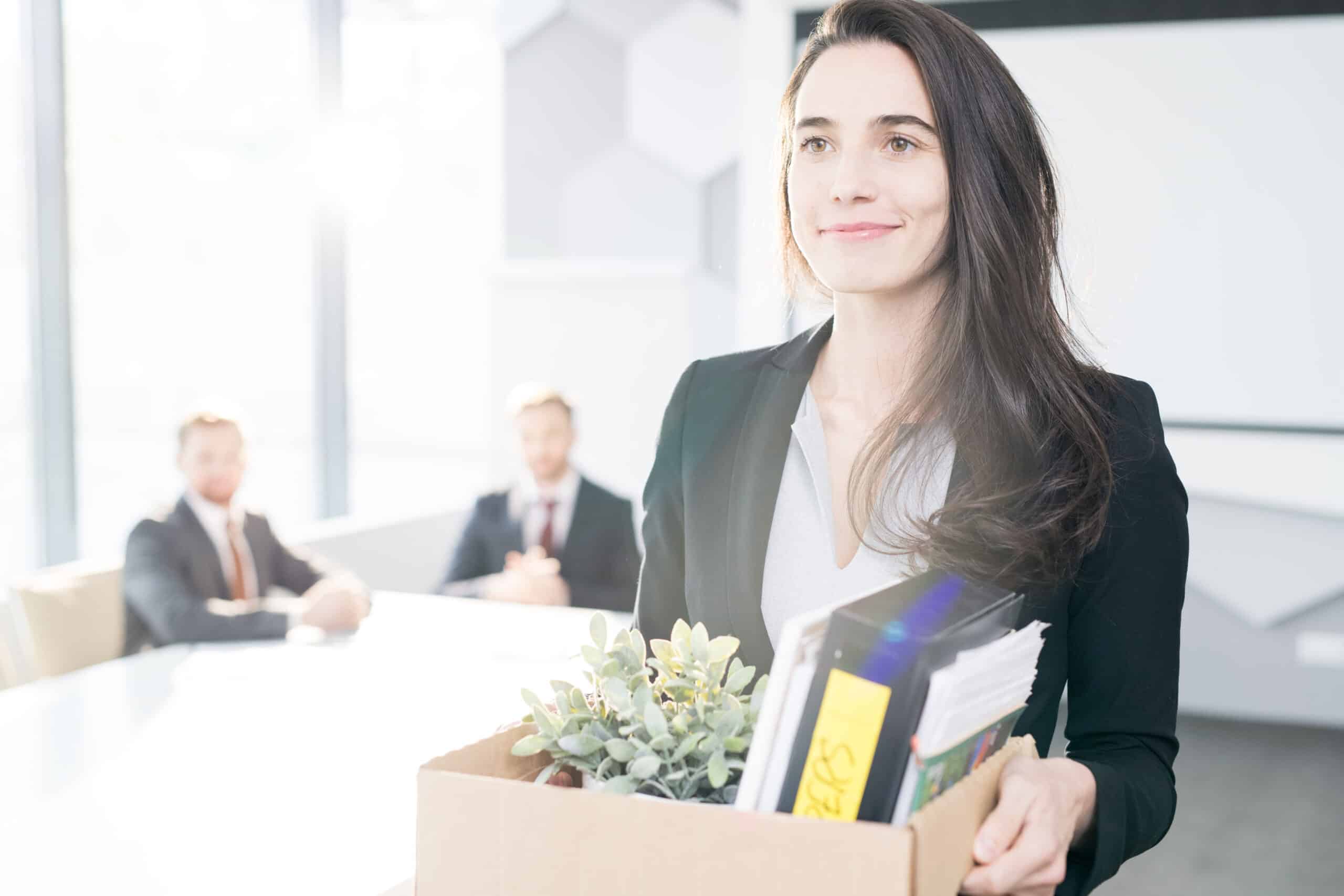 Lächelnde Arbeitnehmerin macht einen Jobwechsel und hält eine Kiste mit persönlichen Sachen in ihren Händen.
