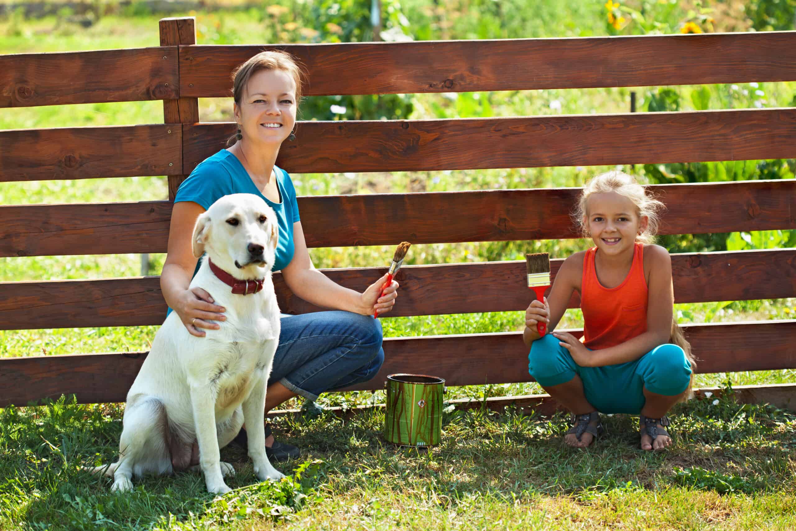 Ein sicherer Garten für den Hund: eine Mutter und ein Kind streichen den Zaun für den Hund im Garten