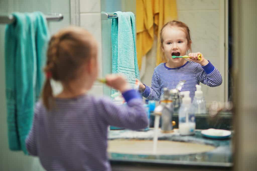 Grinsendes Mädchen putzt ihre Zähne und lässt dabei den Wasserhahn laufen__Apuncto_Energiesparen im Haushalt