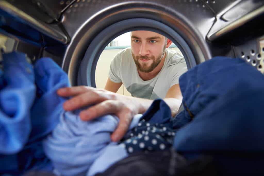 Ein Mann befüllt die Waschmaschine mit Wäsche. Ansicht von innen__Apuncto_Energiesparen im Haushalt