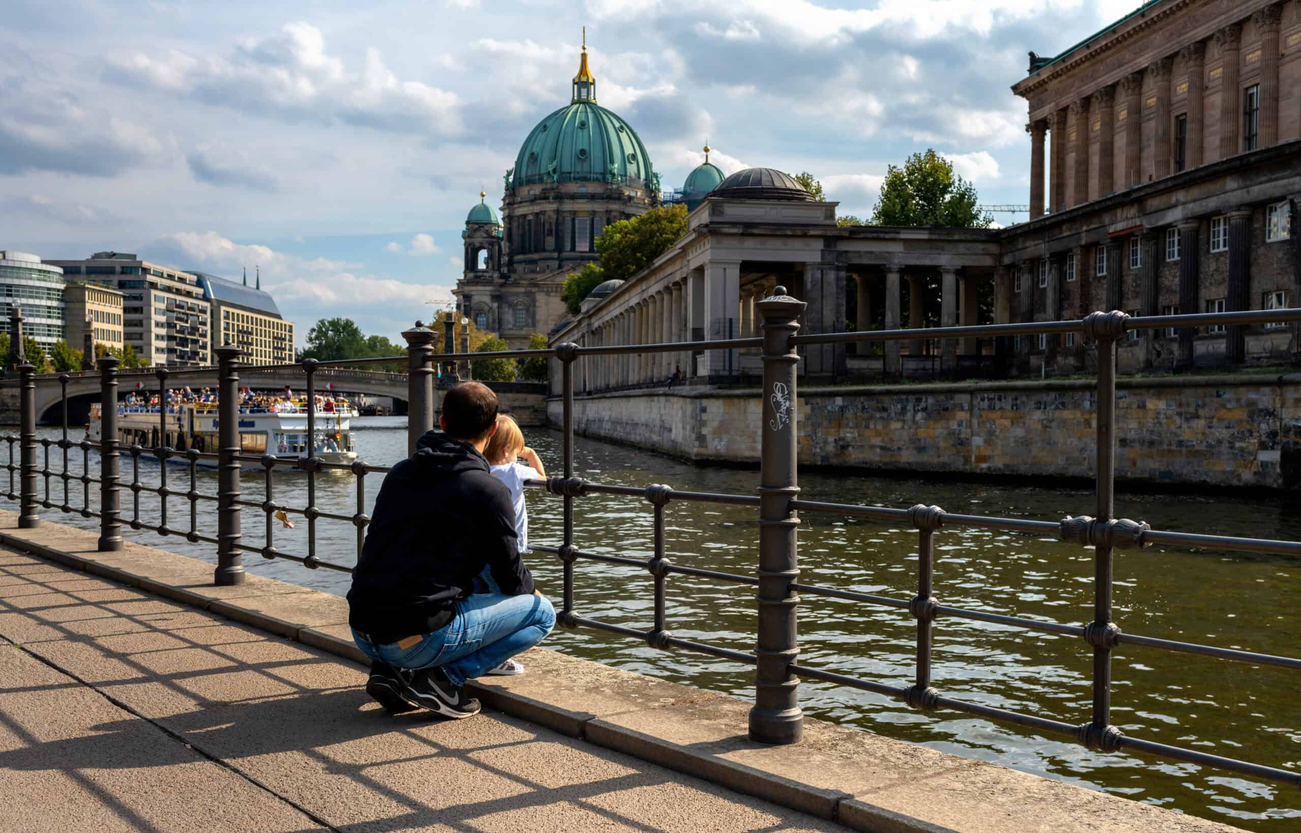 Vater schaut mit Kind in Berlin ein Touristenschiff an. (Berlin Städtetrip)
