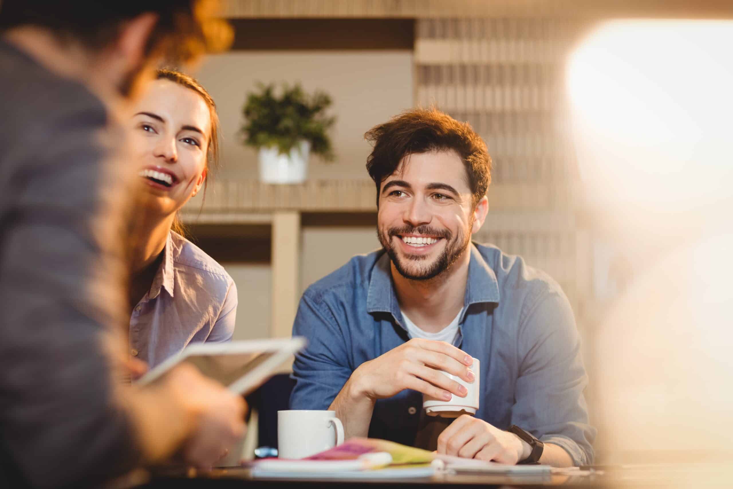 Positive Gedanken im Job: Ein Mann und eine Frau sind in einem Gespräch mit einer weiteren Person. Sie lachen dabei.