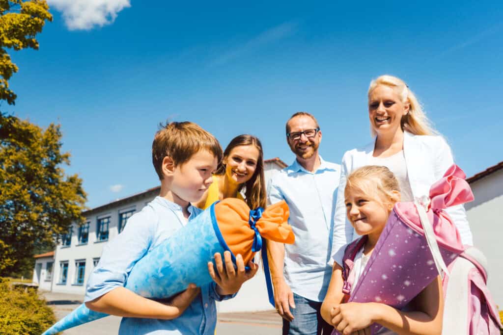 Eine Familie mit Kindern stehen draußen. Die Kinder halten Schultüten in den Händen und sehen glücklich aus.