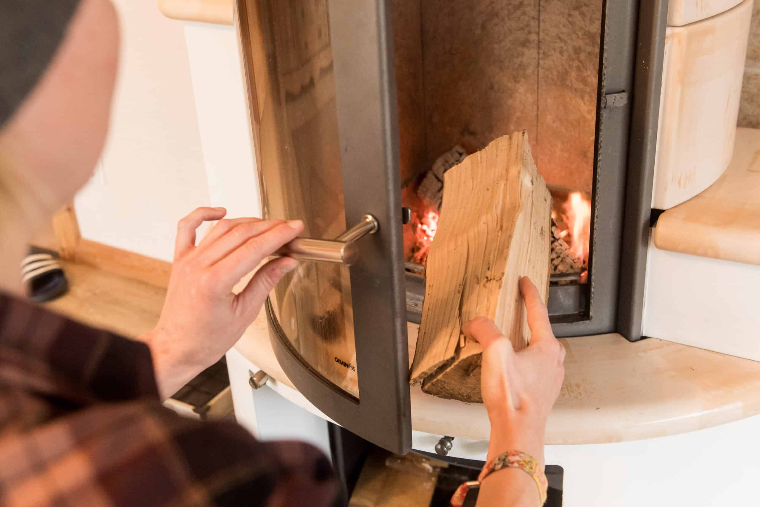 Kamine und Feuerstätten: Das sollten Hausbesitzer wissen Kamine und Feuerstätten: Ein Mann legt ein Stück Holz in den brennenden Kamin nach.