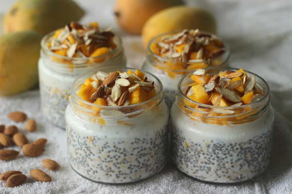Chiapudding mit Mango, gehackten Mandeln und Joghurt in kleinen Gläsern – angerichtet auf einem weißen Tuch